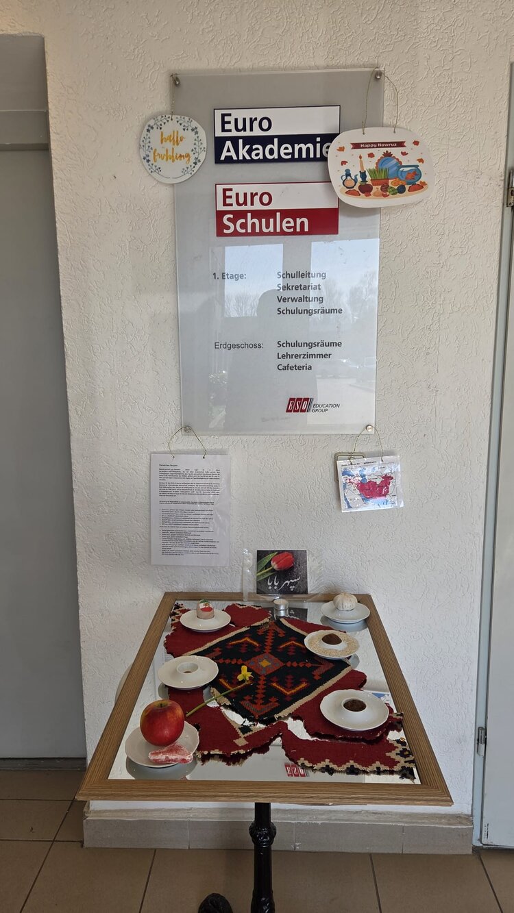 Im Flur der Euro Akademie und Euro-Schulen ist ein kleiner Tisch mit Tischdecke gedeckt, darauf Tellerchen mit verschiedenen Speisen, ein Teelicht und eine Osterglocke.