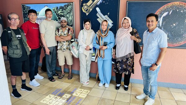 Schülerinnen und Schüler der Euro-Schulen Erfurt stehen vor mehrere Gemälden in bunter Farbe, die Planeten symbolisieren sollen.