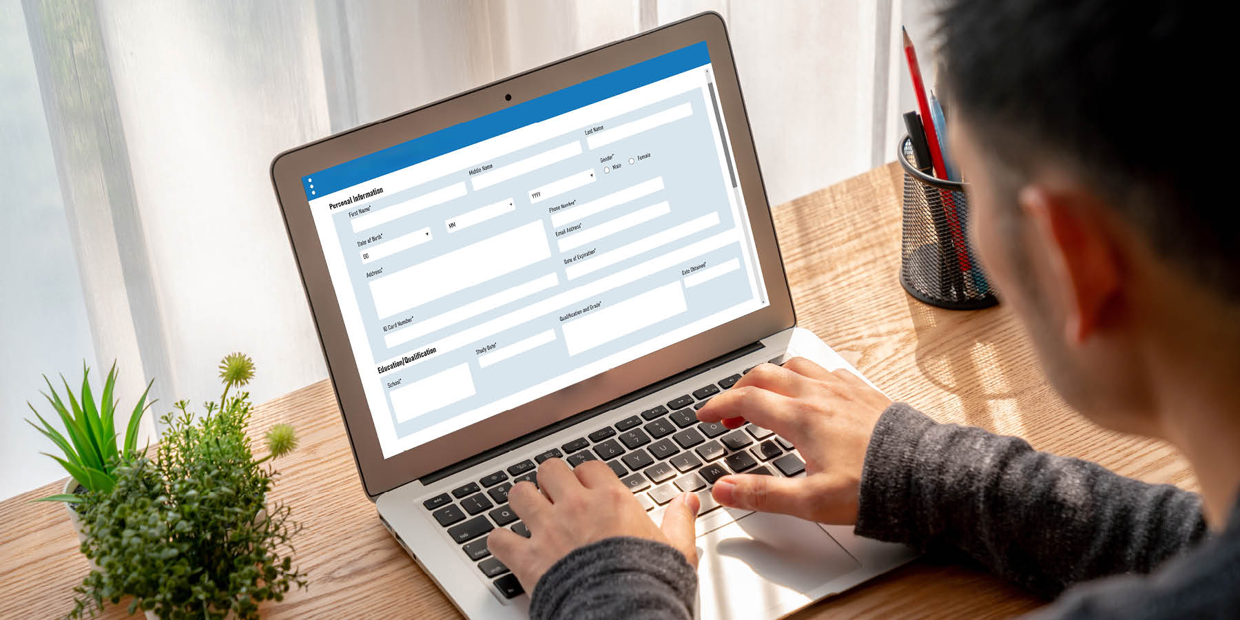 Ein Tisch mit Laptop, auf dem ein Formular gezeigt wird. Ein Mann, den man seitlich von hinten sieht, sitzt vor dem Laptop und tippt.