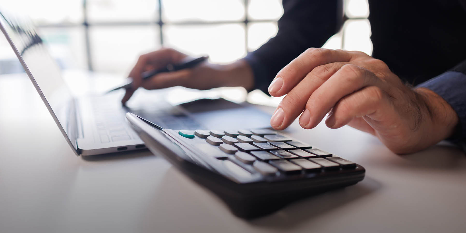 Ein Tisch mit Laptop und Taschenrechner. Zwei Hände, die beide Geräte bedienen.